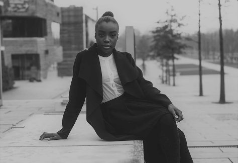 Mujer afro vestida elegantemente, sentada sobre una banqueta en la calle de una ciudad.
