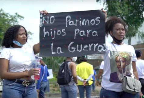 Una mujer y una joven afro en una marcha sostienen un letrero que dice "NO parimos hijos para la guerra"