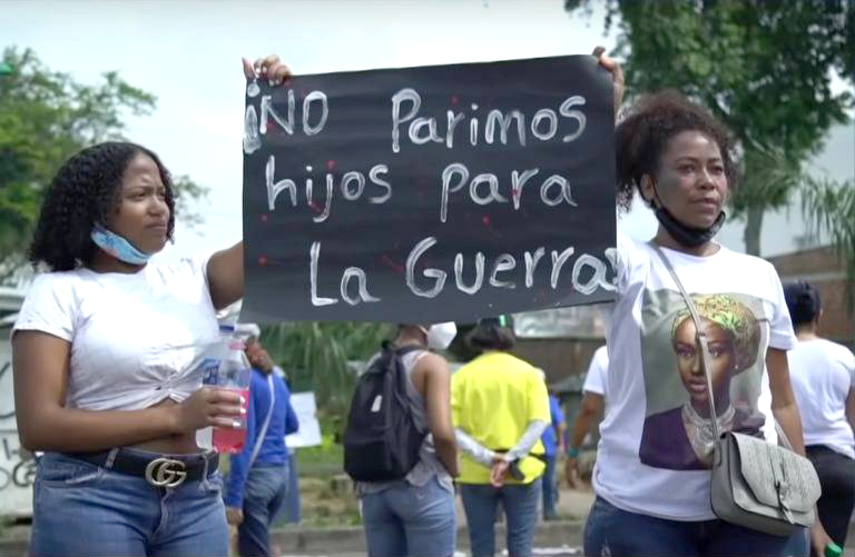 Una mujer y una joven afro en una marcha sostienen un letrero que dice "NO parimos hijos para la guerra"