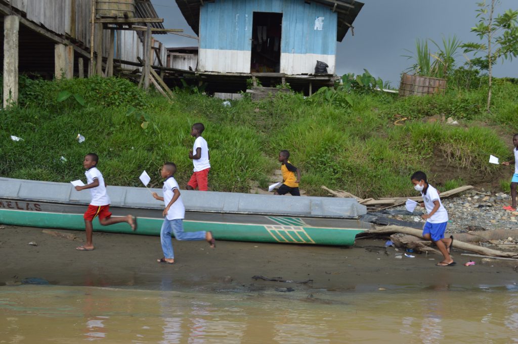Niños corren por la ribera del río junto a canoas al paso de la Caravana por una de las comunidades visitadas