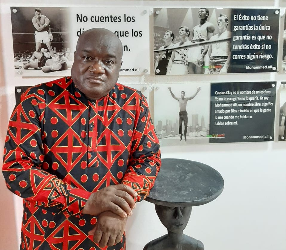 El historiador Sergio Mosquera posa con una camisa de manga larga de diseños africanos y con el codo apoyado en una figura de madera de origen africano. Detrás de él se ven postales sobre Mohammad Alí en el Centro Muntu Bantú.