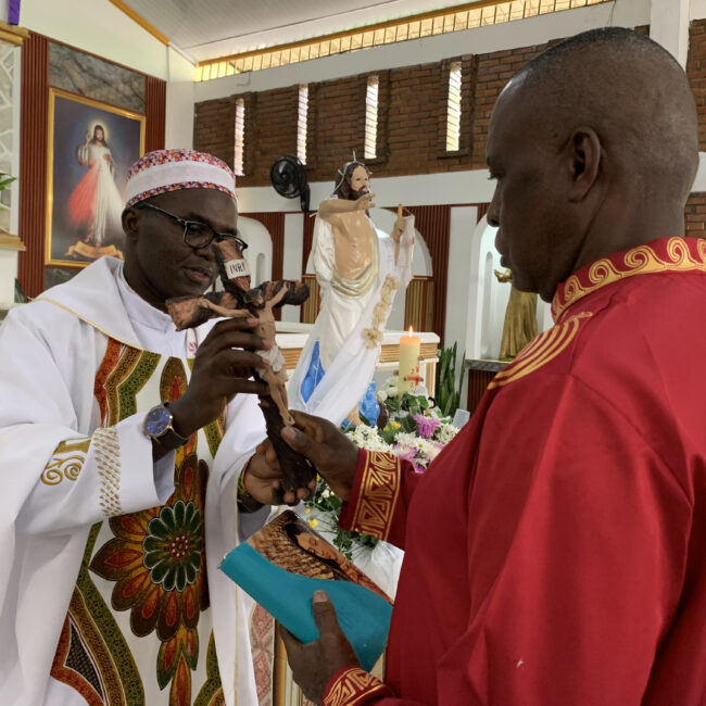 El p. Elías Libanda imc, delegado de Pastoral Afro Cali, entrega el crucifijo a Ferneyz Carabalí, mientras este laico misionero de la Consolata sostiene una biblia. Al fondo se ve la imagen de Cristo Resucitado en el templo de Cristo Maestro.