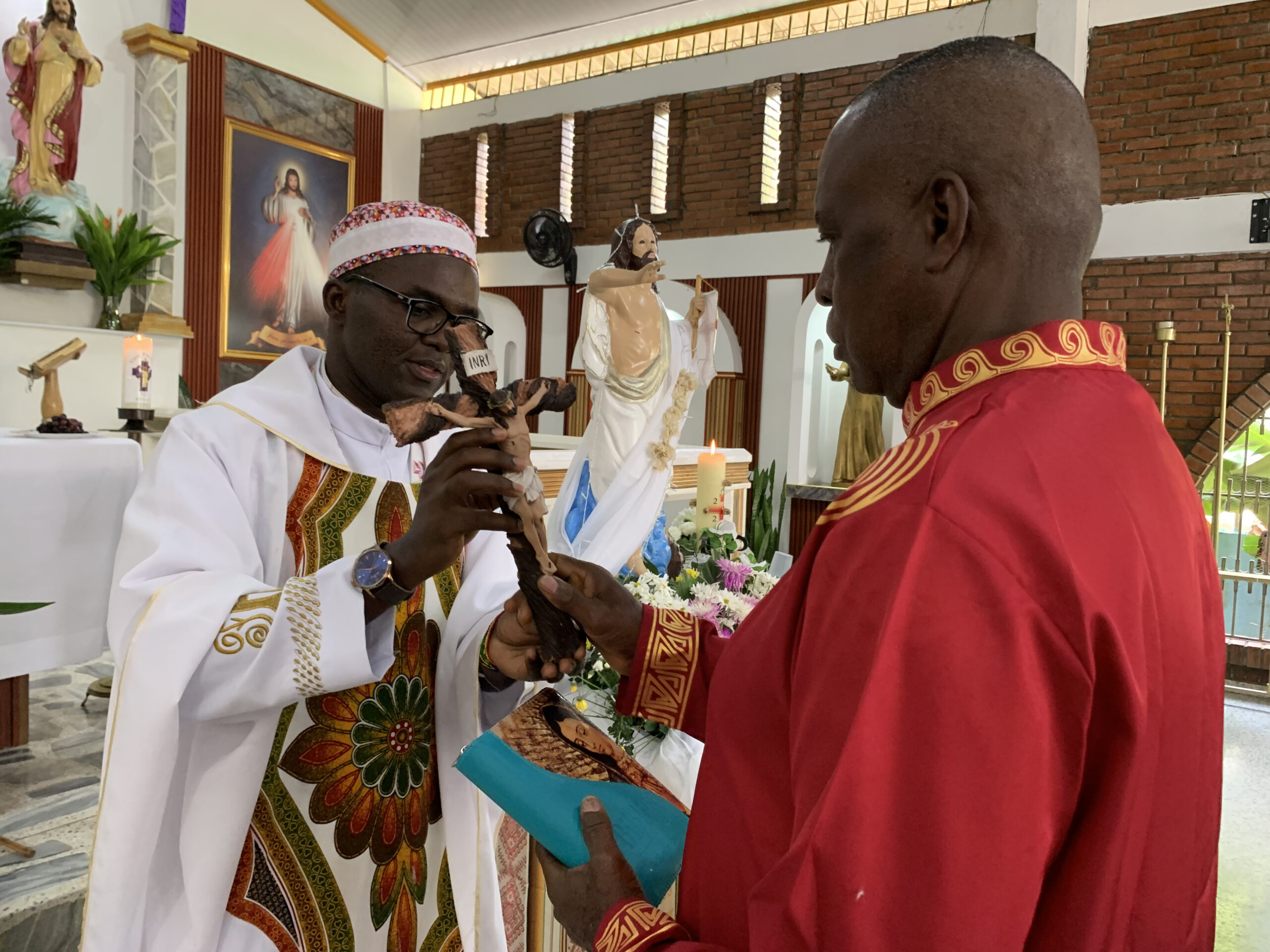 El p. Elías Libanda imc, delegado de Pastoral Afro Cali, entrega el crucifijo a Ferneyz Carabalí, mientras este laico misionero de la Consolata sostiene una biblia. Al fondo se ve la imagen de Cristo Resucitado en el templo de Cristo Maestro.